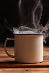 Mug with smoke, white coffee mug on rustic wood releasing smoke, dark background, selective focus.