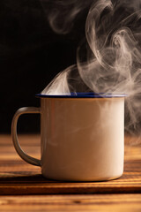 Mug with smoke, white coffee mug on rustic wood releasing smoke, dark background, selective focus.