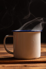 Mug with smoke, white coffee mug on rustic wood releasing smoke, dark background, selective focus.