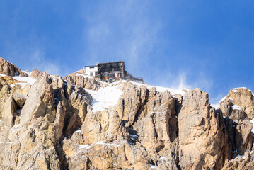 Low angle view of a cable car top station on snow covered rocky mountain peak on a windy winter day
