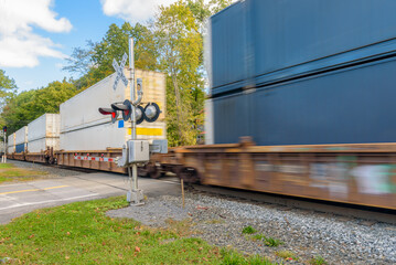 Fast moving container train passing a railroad crossing on a sunny autumn morning