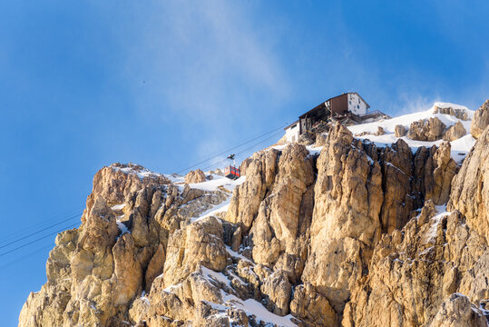 Aerial tramway passenger cabin approaching the higher station on the top of a snowy rocky peak  in the Alps on a clear winter day