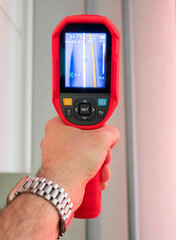 A thermal imaging camera held in the man hand on a warm radiator pipe. Close up vertical image.