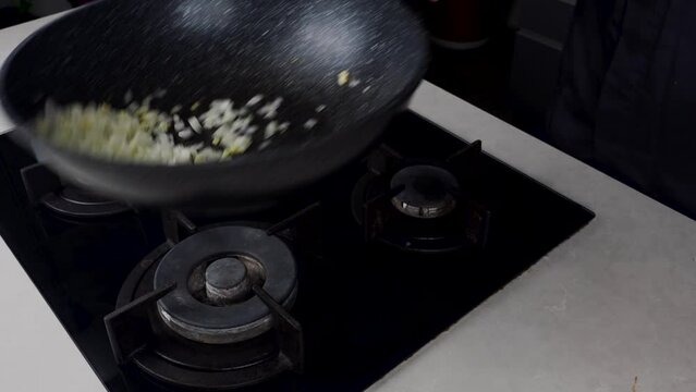 Close up of Chef cook hands cooking and toss roasted onion and garlic in frying wok pan on gas stove. Flying food levitation. 