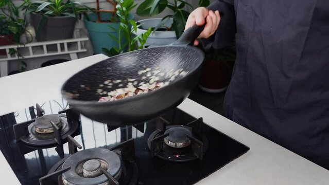 Close up of Chef cook hands cooking and toss roasted onion and garlic in frying wok pan on gas stove. Flying food levitation. 
