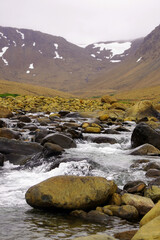Stream tumbling over rocks in the foreground with desolate mountain slopes in the background in the...