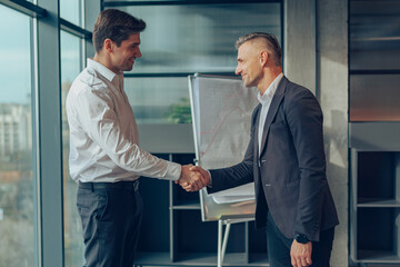 Two business people shaking hands after successful partnership negotiation in office