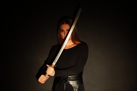 Beautiful woman in black holding old katana sword