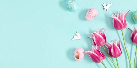 Easter decorations concept. Top view on pink tulips flowers, colorful eggs on pastel blue...