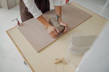 Close up of f woman preparing clay to create a mug on a wooden table in pottery studio