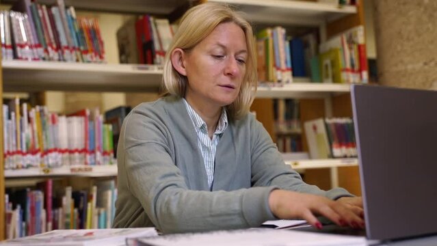 Middle aged woman typing on keyboard using laptop in public place, coworking. Business or freelancer working remotely. Adult student studying in public library Technology in education and business