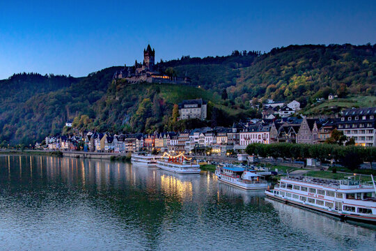 The quaint, peaceful medieval village town of Cochem, Germany, on the Moselle River at sunset with the Cochem Reichsburg Castle on top of the hill.