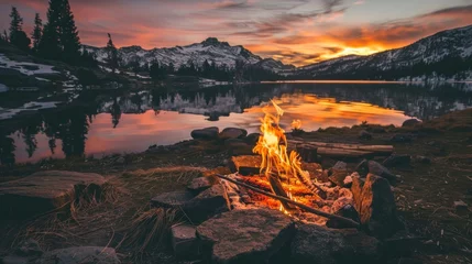Zelfklevend Fotobehang majestic landscape with a large campfire on the ground next to a lake and large mountains on a sunset © Marco