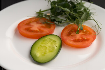 Sliced tomatoes and cucumber on a white plate with a garnish of pea shoots.