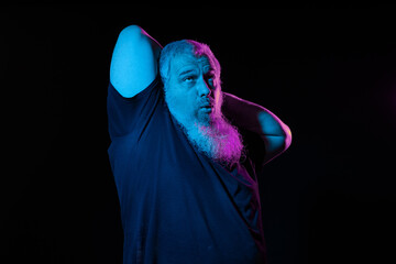 A bearded man looks puzzled with one hand behind his head, highlighted by contrasting neon lights.