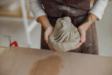 Close up of female potter in apron kneads piece of clay with her hands on table in studio