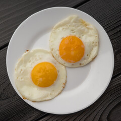 A white plate with two fried eggs and a sausage on a dark wooden surface.