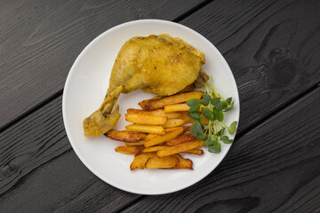 A roasted chicken leg with fries and micro green on a white plate