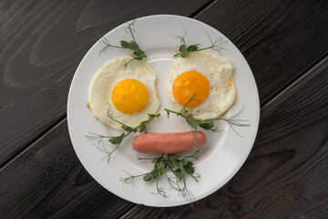 Breakfast of fried eggs and a sausage on a white plate, garnished with fresh microgreens.