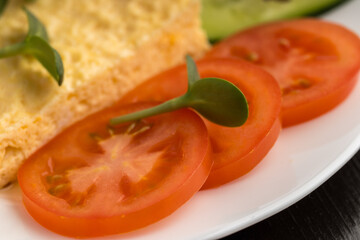 Close-up of an omelette with tomatoes and a microgreen on a white plate