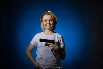 Smiling woman in a hat with a gun on a dark background.