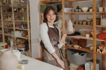 Smiling entrepreneur crafts woman holding mug in pottery studio while looks away 