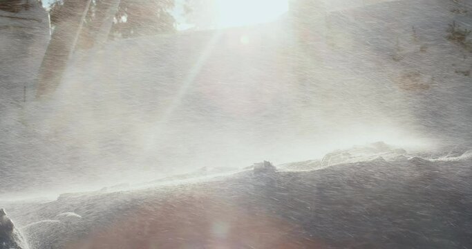 A strong wind whirls the snow into the air in the rays of sunlight