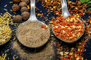Spices lie on two teaspoons on a black background next to peppercorns and food close-up	
