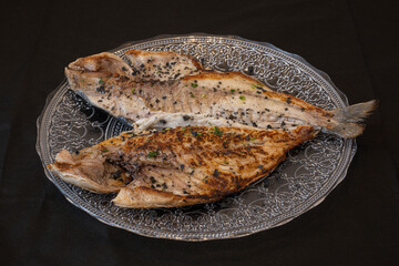 Grilled opened gilt-head bream on glass plate with parsley