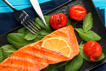 Tasty grilled salmon with tomatoes, spinach and lemon served on table, top view