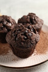 Delicious chocolate muffins and cacao powder on light grey table, closeup