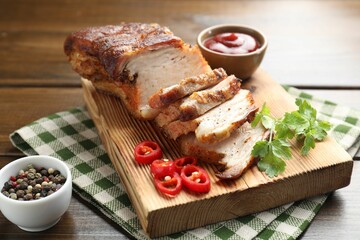 Pieces of baked pork belly served with sauce, chili pepper and parsley on wooden table, closeup