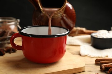 Pouring tasty hot chocolate into cup at wooden table, closeup