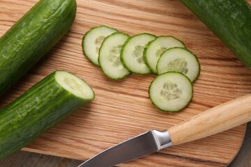 Cut cucumber and knife on wooden board, top view