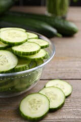 Cut cucumber in glass bowl on wooden table, closeup