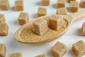 Brown sugar cubes in spoon on white wooden table, closeup