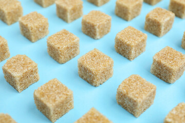 Brown sugar cubes on light blue background, closeup