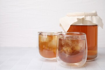 Tasty kombucha with ice cubes on white tiled table, space for text