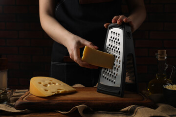 Woman grating cheese at wooden table, closeup