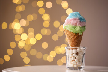 Sweet cotton candy in waffle cone on table against blurred lights, closeup. Space for text
