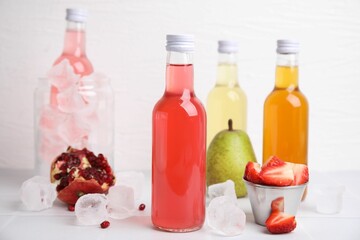 Tasty kombucha in glass bottles, fresh fruits and ice on white table