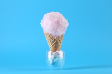 Sweet cotton candy in waffle cone on light blue background