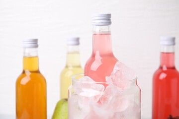 Tasty kombucha in bottles and glass with ice on white background, closeup