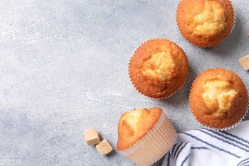 Delicious sweet muffins and brown sugar on light grey textured table, flat lay. Space for text