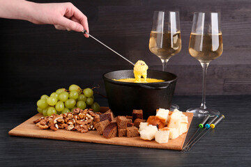 Woman dipping piece of bread into fondue pot with melted cheese at black wooden table, closeup