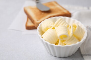 Tasty butter curls in bowl and toasts on light grey table, closeup. Space for text