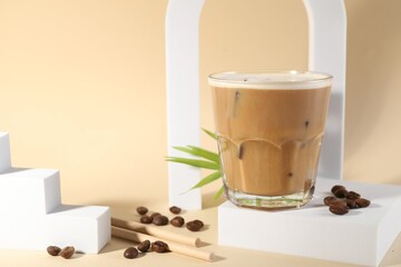 Refreshing iced coffee with milk in glass and beans on pale yellow background, space for text