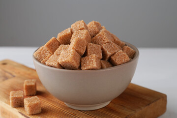 Brown sugar cubes in bowl on white table, closeup