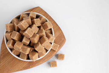 Brown sugar cubes in bowl on white background, top view. Space for text