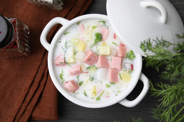 Delicious cold summer soup (okroshka) with boiled sausage in pot on grey wooden table, top view